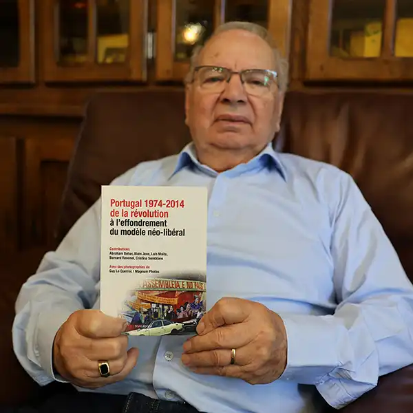 Portrait d'Américo qui tient fièrement dans ses mains un livre : "Portugal 1974-2014 de la révolution à l'effondrement du modèle néo-liébral"