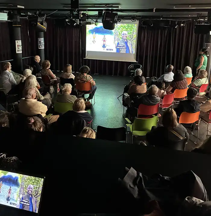 rassemblements de tous les participants et toutes les participantes de dos assis sur des chaises. En devant de scène, le visuel du reste de son âge est projeté sur un écran. Tout le monde écoute attentivement.